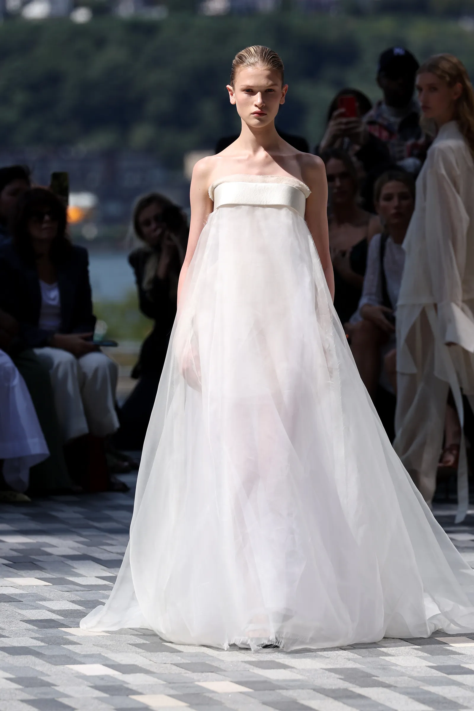 A model in a long white gown walks on a runway.