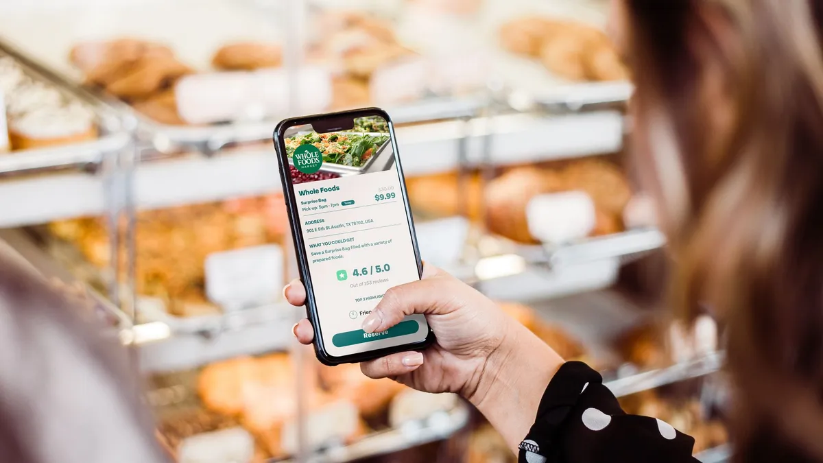 Shopper using Too Good To Go app inside Whole Foods' store in front of bakery section