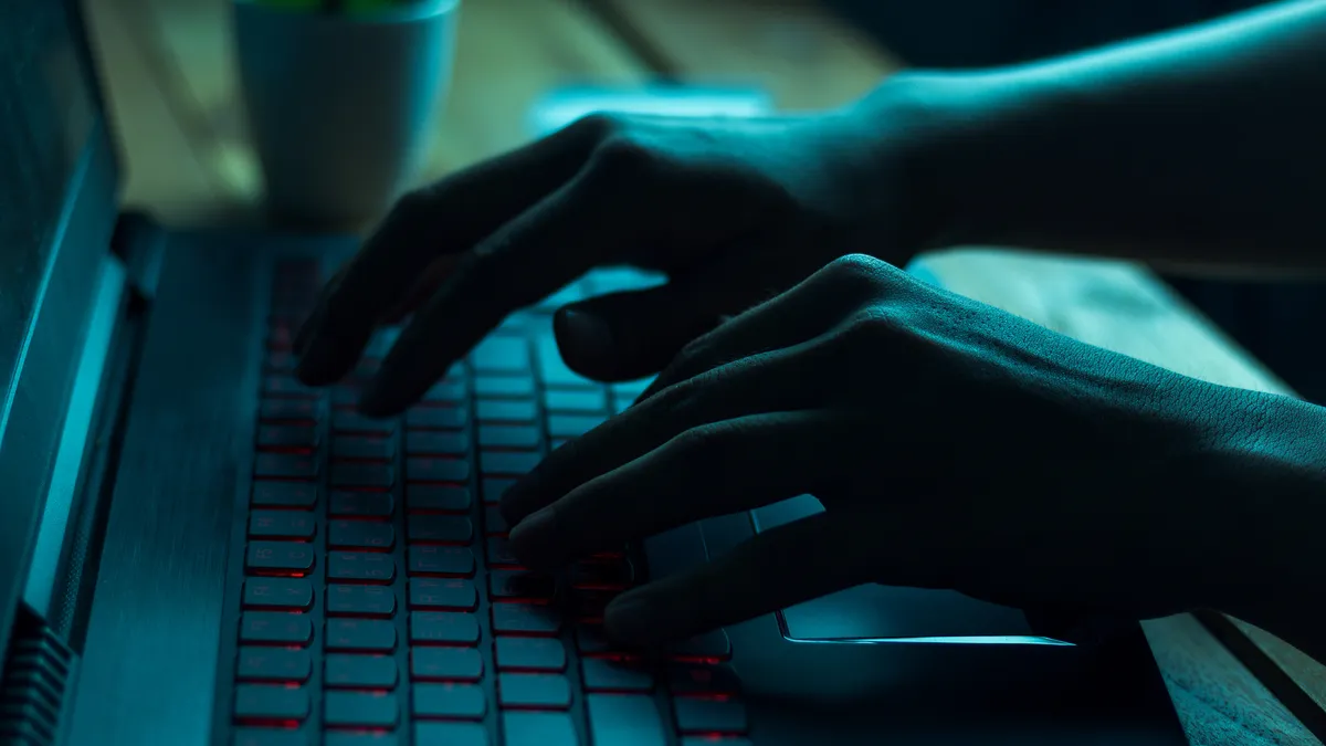 A person types on a laptop in a dark room.