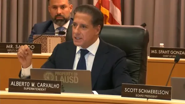 Alberto Carvalho speaks while sitting at a table during a school board meeting.
