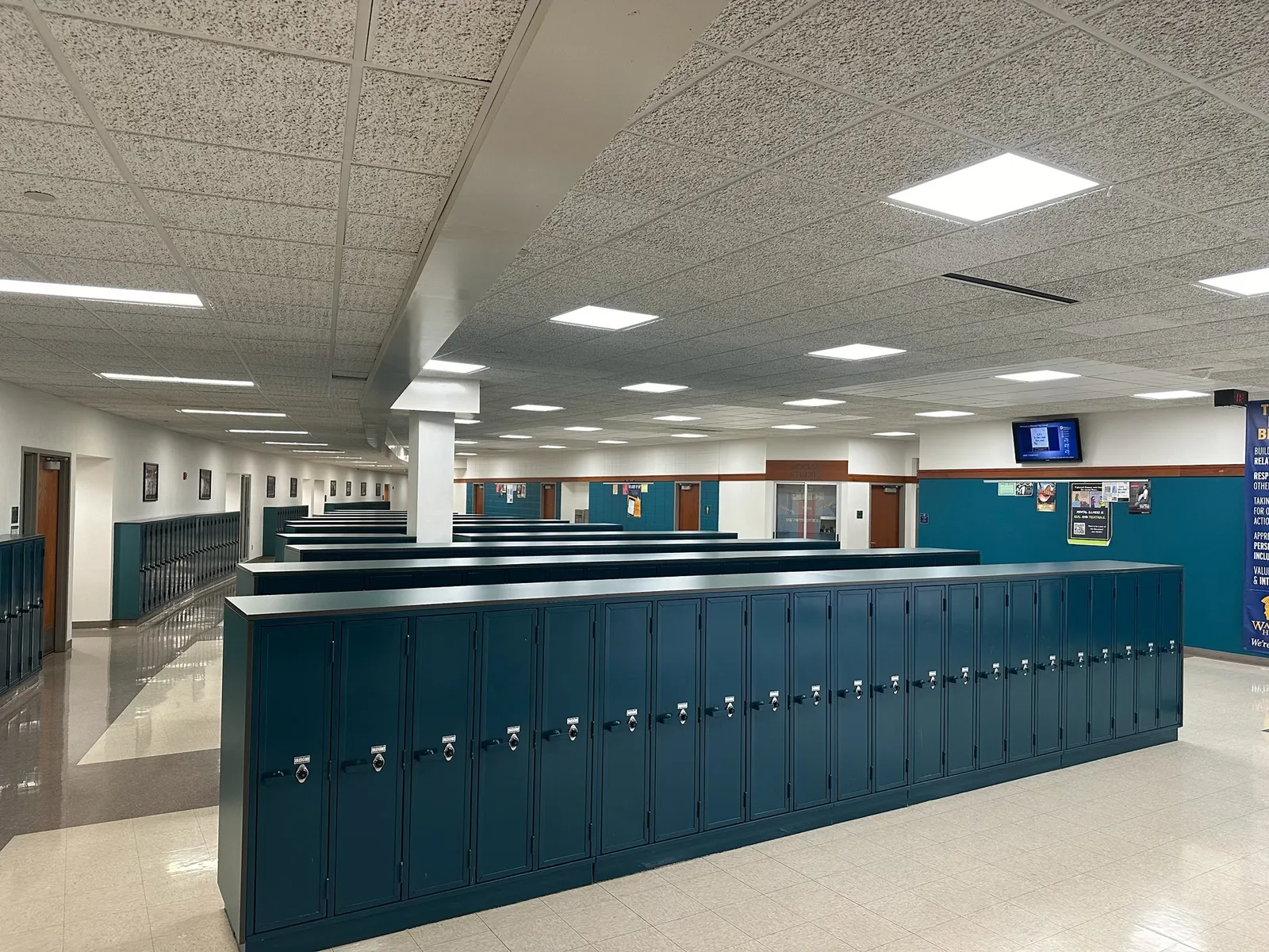 Rows of floor-to-waist-high lockers sit in a hallway in a school.