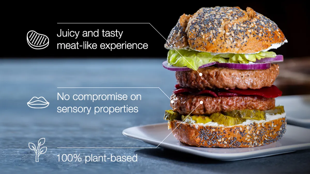 A double-decker plant-based burger with pickles, red onions, mayonnaise, and red round slices on a poppy and sesame seed bun, with words explaining the ingredients.