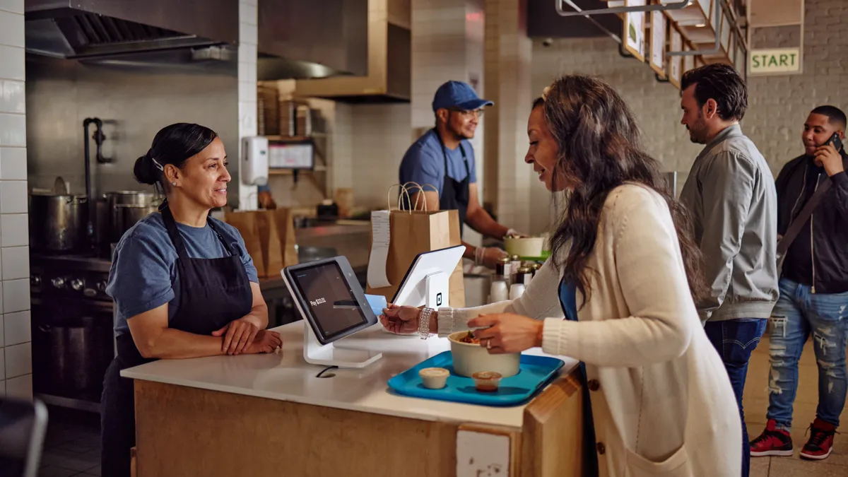 A restaurant customer using a card to pay via a Square tap device at the counter.