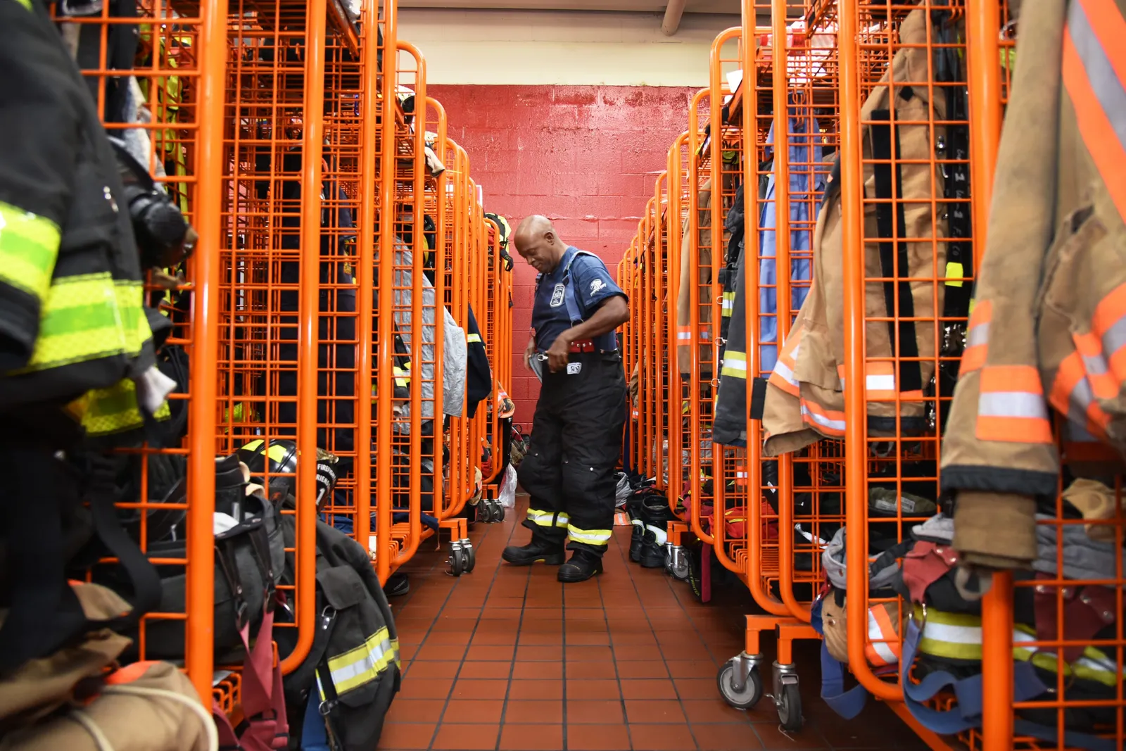 A person putting on firefighter trousers in the center, with rows of firefighter protective gear hanged on the left and right side.