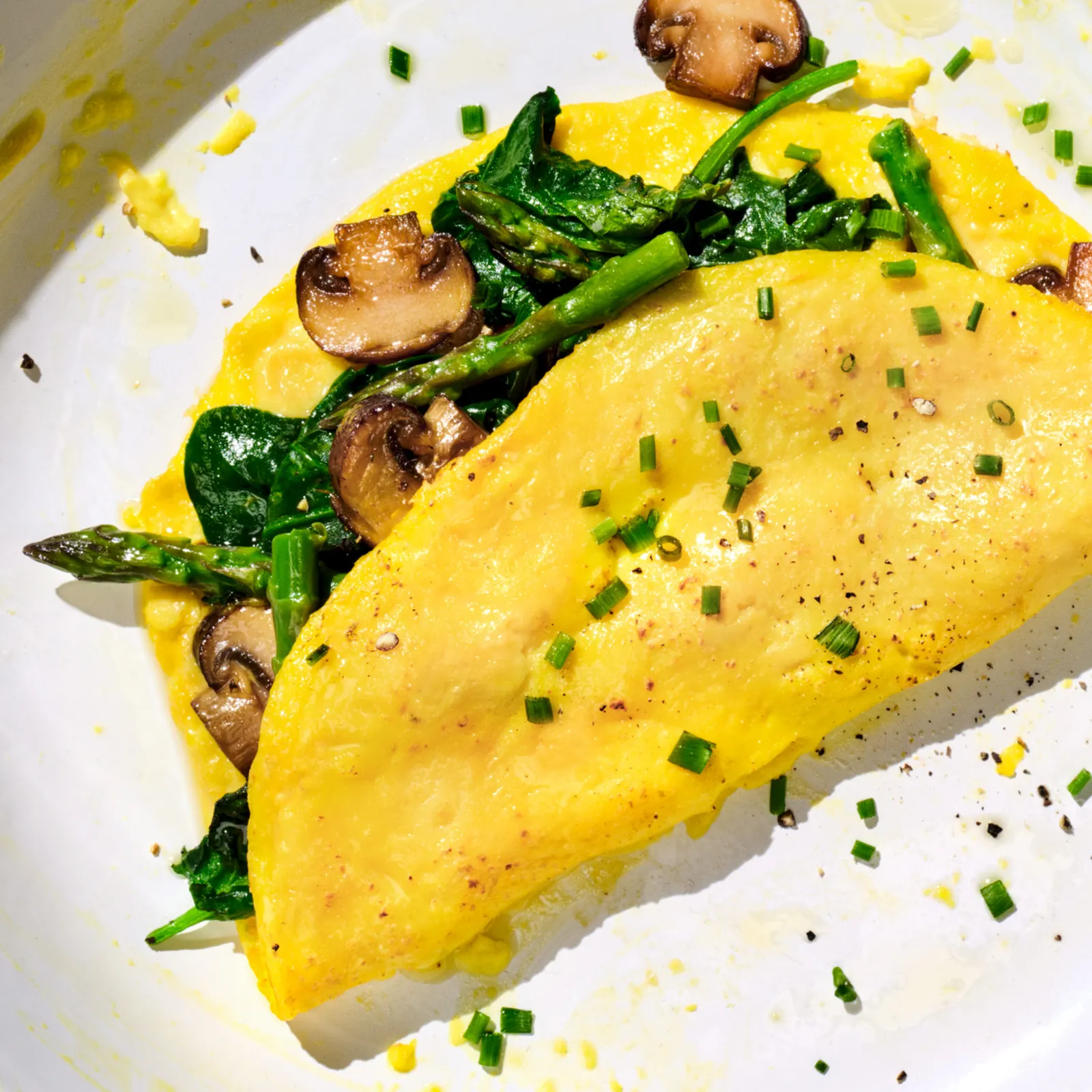 An omelet stuffed with greens, artichokes and mushrooms, with chopped chives sprinkled on top, sits on a white plate.
