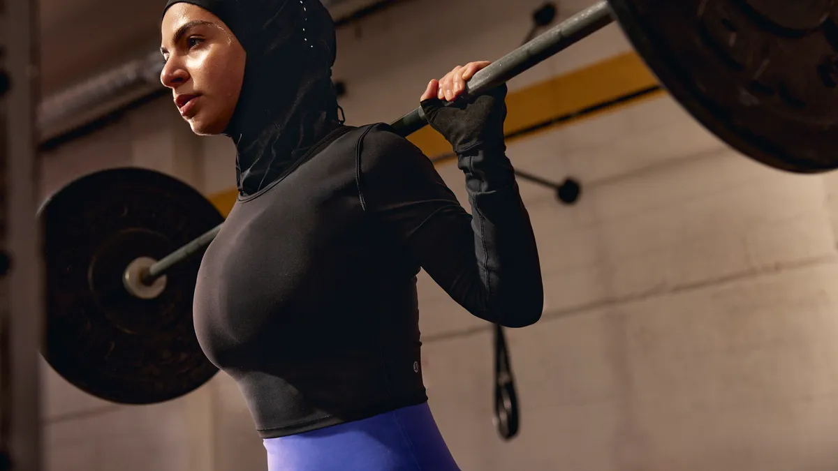 A woman lifting a barbell while wearing a hijab from Lululemon