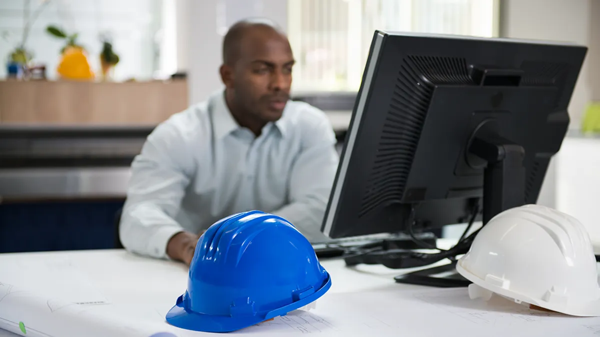 Construction protective helmets with blurred image of engineer working on computer in the background.