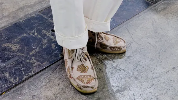 A person wears beige pants and printed beige shoes.