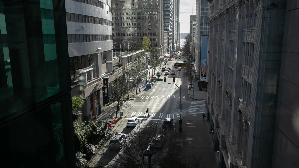 An elevated shot of a street lined with high-rise buildings. One person walks across a crosswalk.