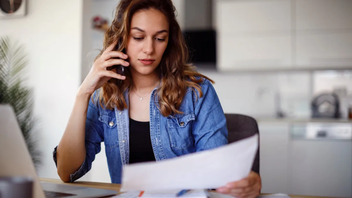 A person looking down at a piece of paper while on the phone