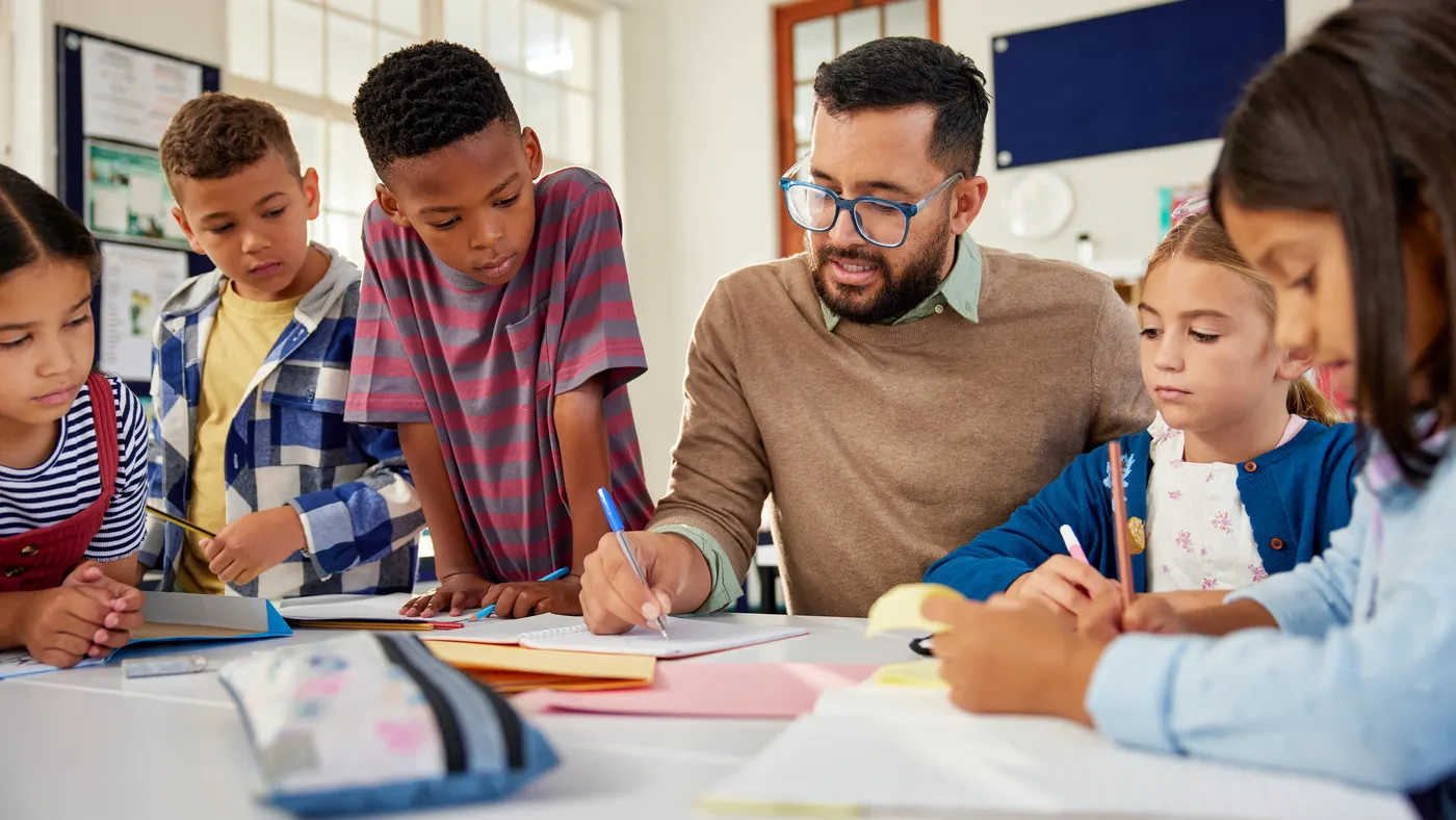 Young school teacher helping elementary students while writing in notebooks