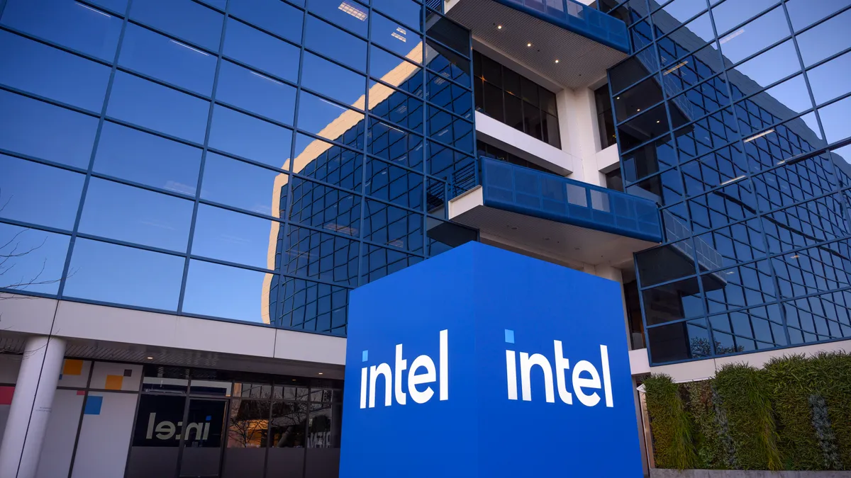 A lit blue block with "Intel" in white letters placed in front of a building with reflective windows.