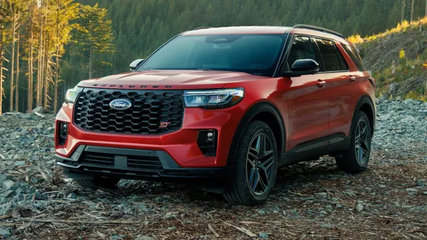 A red 2025 Ford Explorer SUV parked outdoors with a forested mountain in the background.