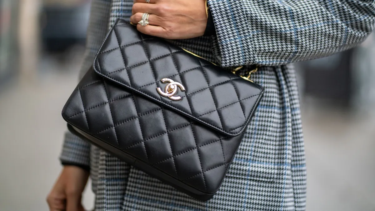 A person in a black-and-white checked suit carries a black quilted bag.