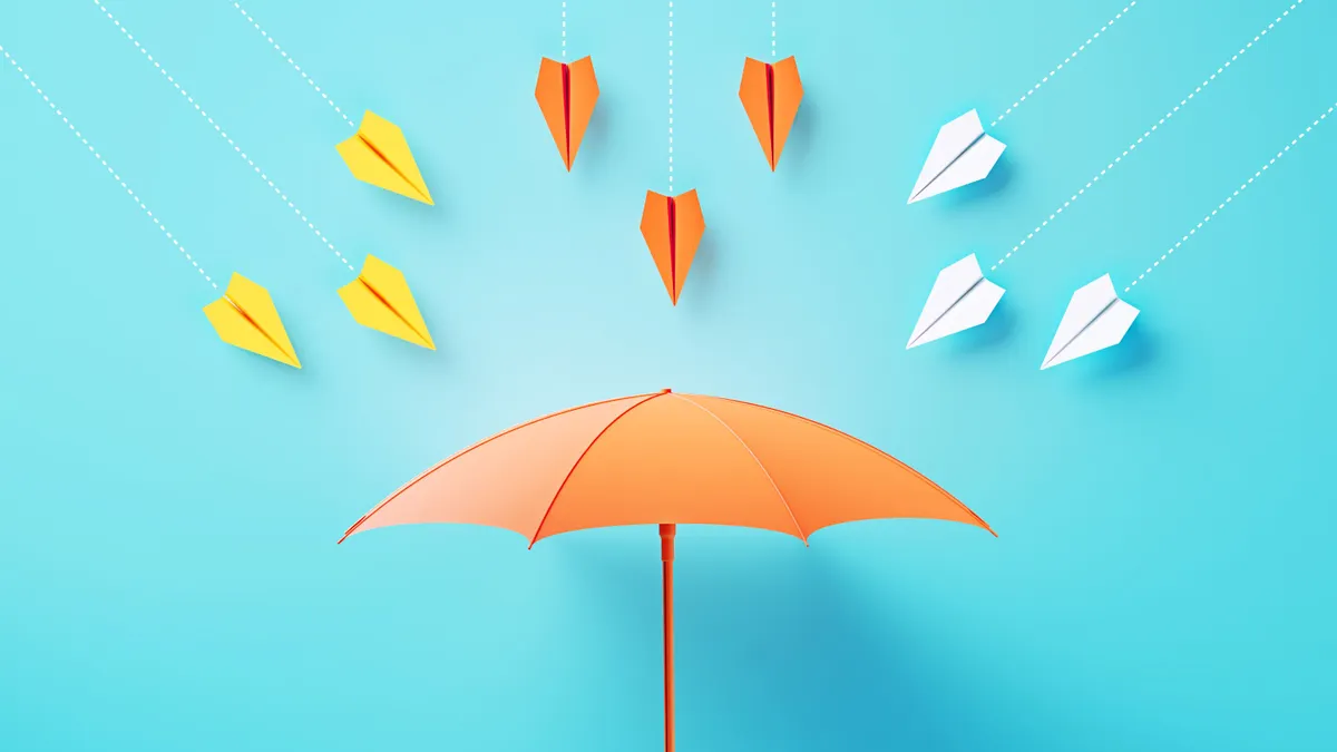 Yellow, orange and white paper planes flying toward a coral colored umbrella on blue background.