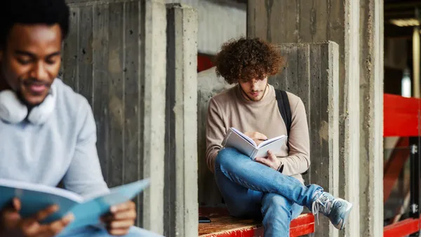 Two people sit on different benches while reading.