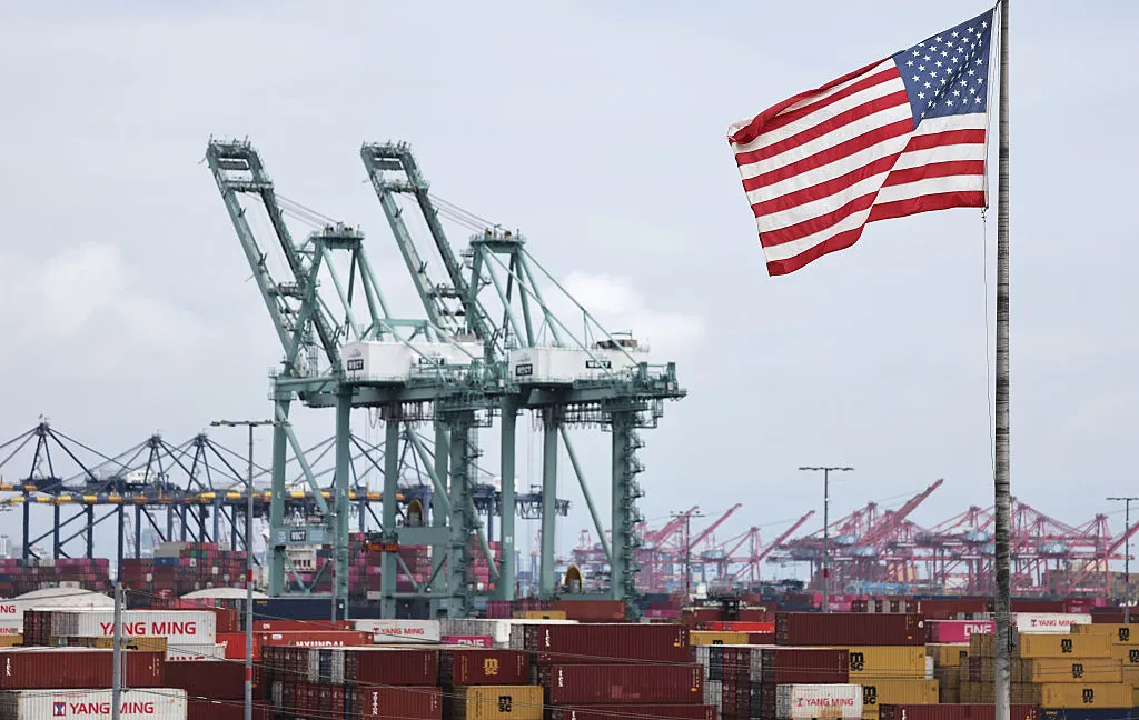 An American flag flies in front of shipping containers and cranes at the Port of Los Angeles on September 26, 2025 in Los Angeles, California.