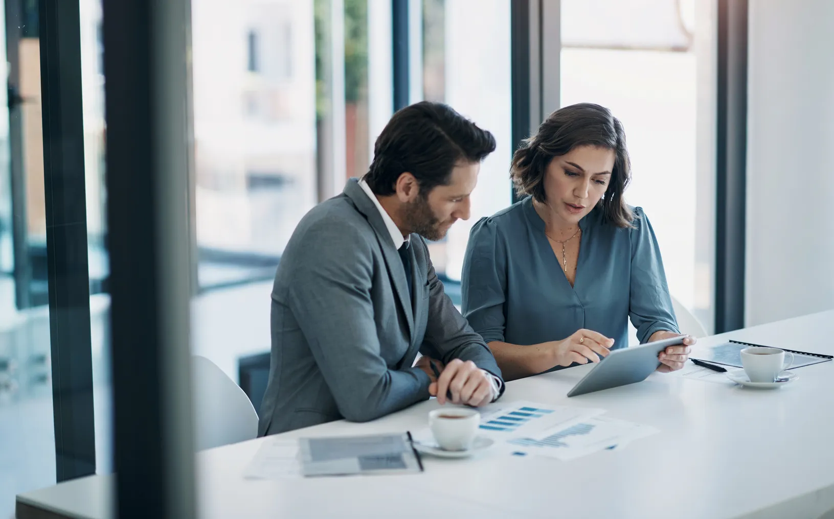 Business people sit at a table in an office planning budgets using a tablet and charts.