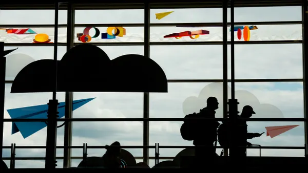 Two passengers walk through an airport as one looks at a phone.