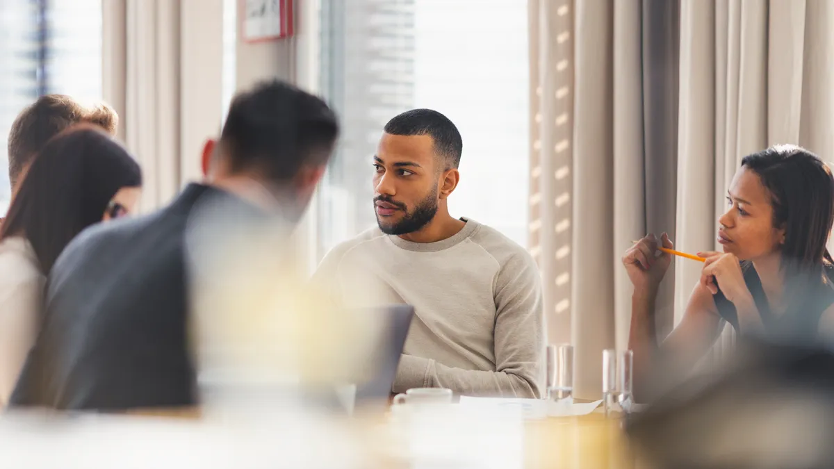 Five people sitting at a table with coffee and computers. Two of the people in focus, the other three have their backs toward the camera.