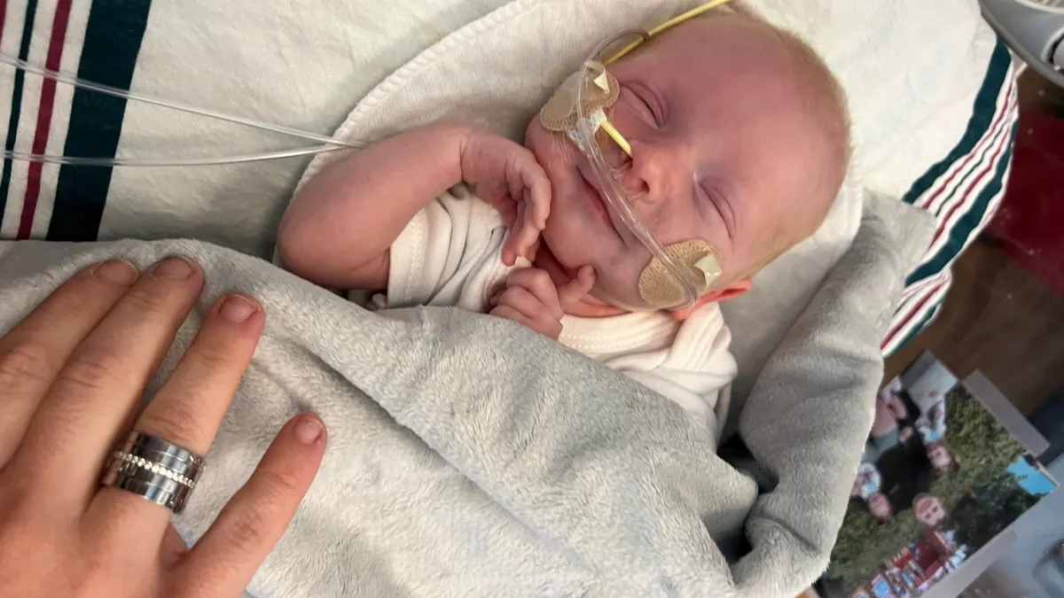 A swaddled infant in a hospital bassinet smiles.