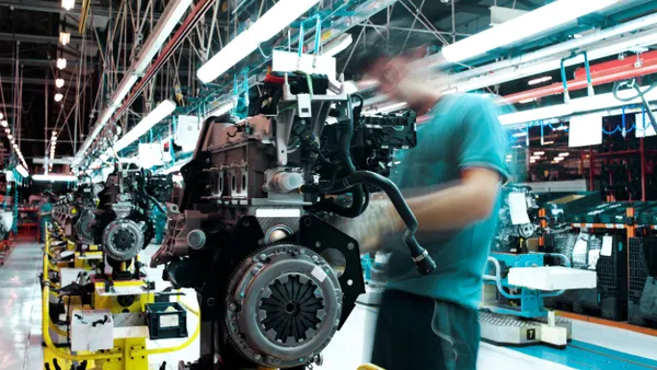 A person whose upper body is blurred as they work on an engine inside a factory.