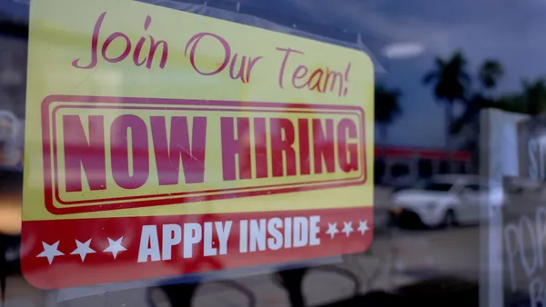 A hiring sign in a window that reads "Join our team! Now hiring. Apply inside."