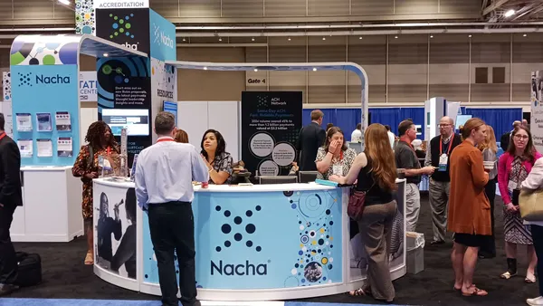 People milling at a conference in front of a booth that says Nacha.