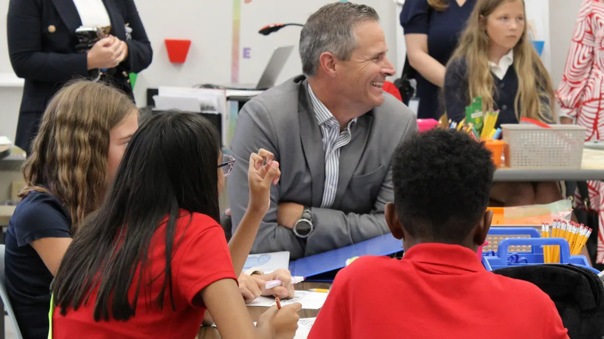 A man in a gray suit sits among children