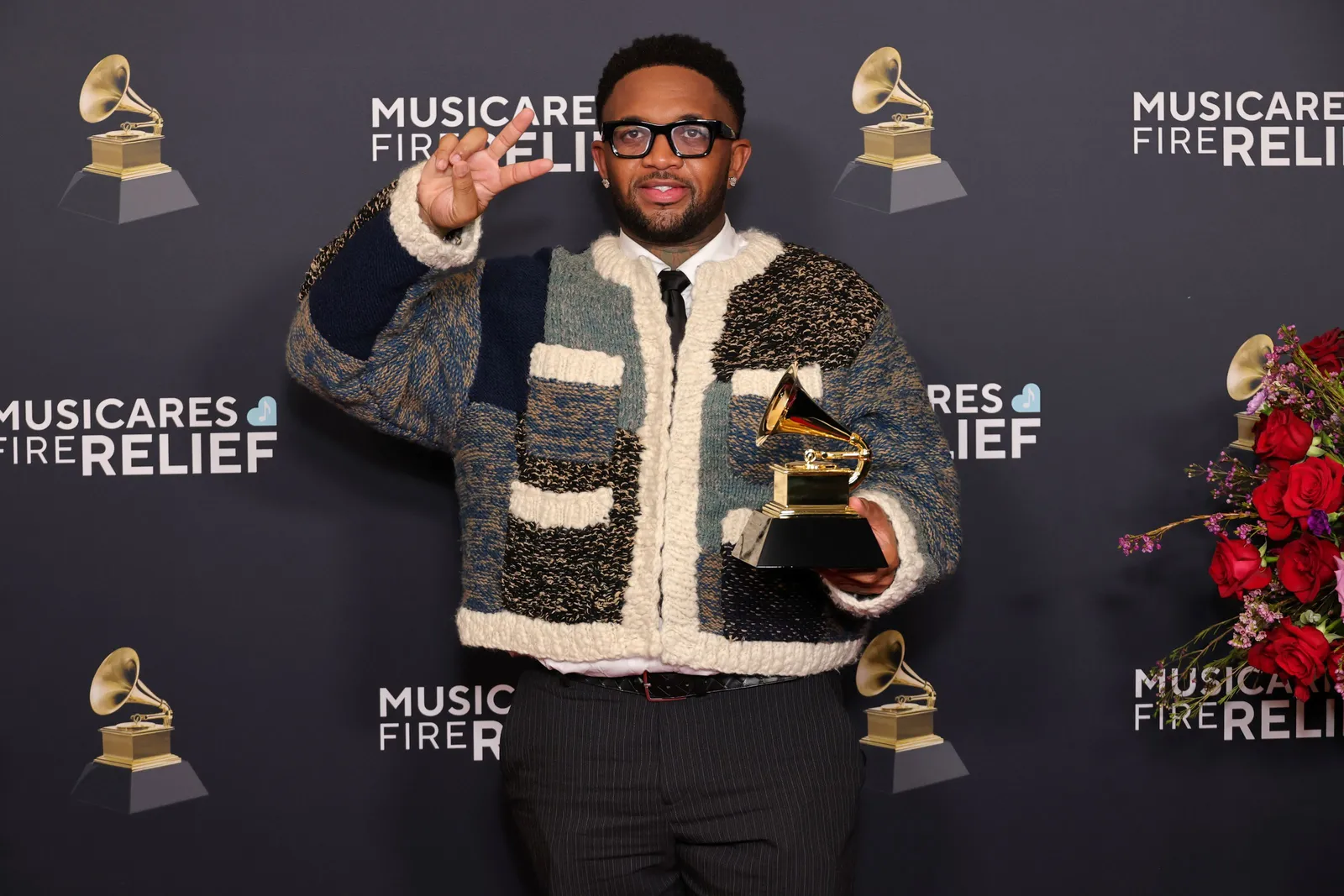 A person wears a chunky knit sweater and holds a Grammy award.