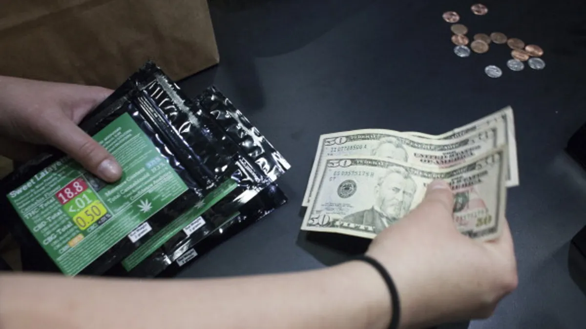 An employee collects money while holding packages of marijuana