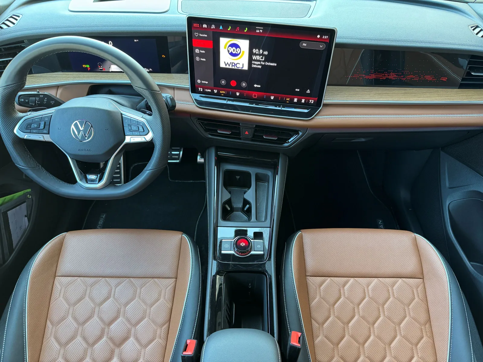 An overhead shot of the VW Tiguan SEL R-Line’s driver-oriented cabin. Stainless-steel-capped pedals, a racing-inspired steering wheel and cockpit-like layout that embraces the driver signals the cabin’s design intent. The amber-brown leather that splashes color from the seats to the doors and dash provides a finishing punch.