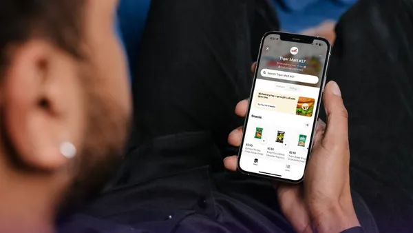 A photo of a person sitting in a chair looking at a mobile phone with a delivery app open. The app says Tiger Mart.