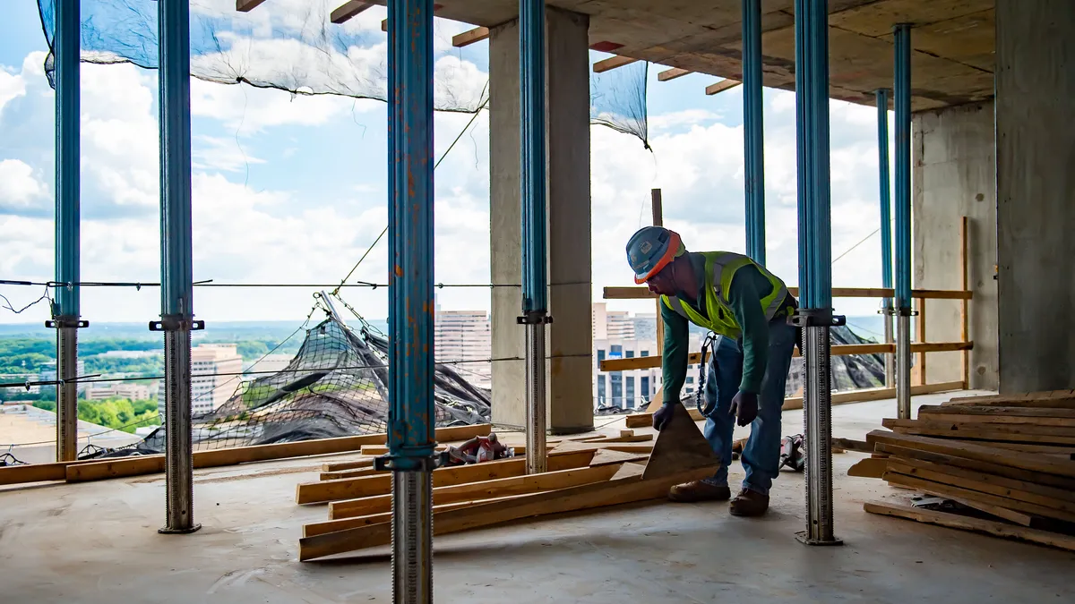 A worker bends over to life some materials several floors up in a building under construction.