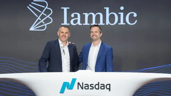 A picture of two Iambic Therapeutics executives smiling in front of the Nasdaq logo