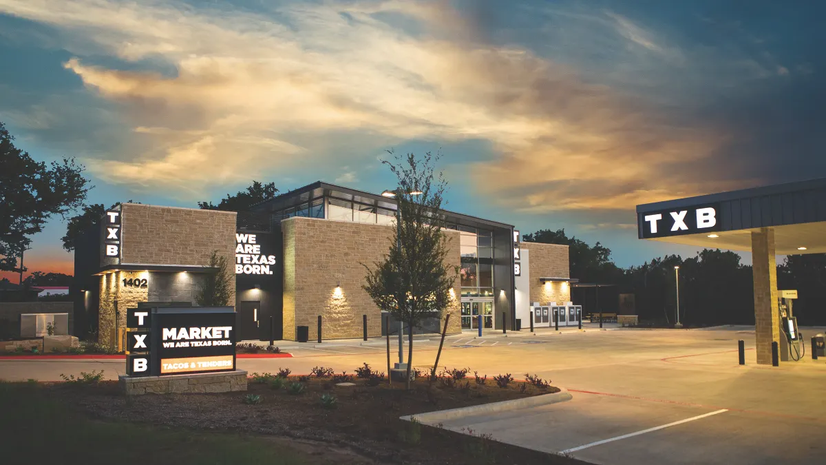 A photo of a store at sunset. A sign out front says "TXB Market. We are Texas Born. Signs on the building and fuel canopy say TXB and another sign on the store says We Are Texas Born.
