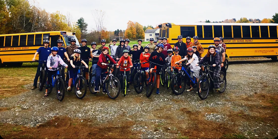 A group of students stand with bikes outside in front of two school buses