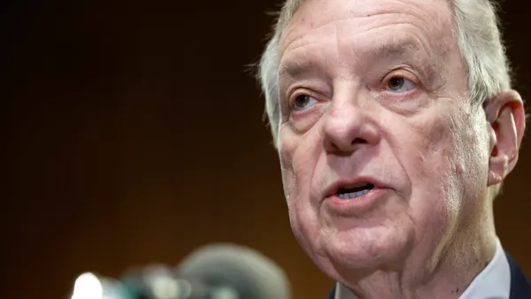 An elderly person in a suit speaking into a microphone.