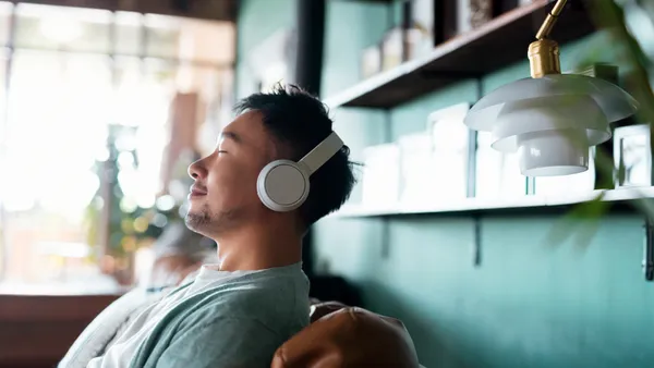 A person with eyes closed, enjoying music over headphones while relaxing on a sofa.