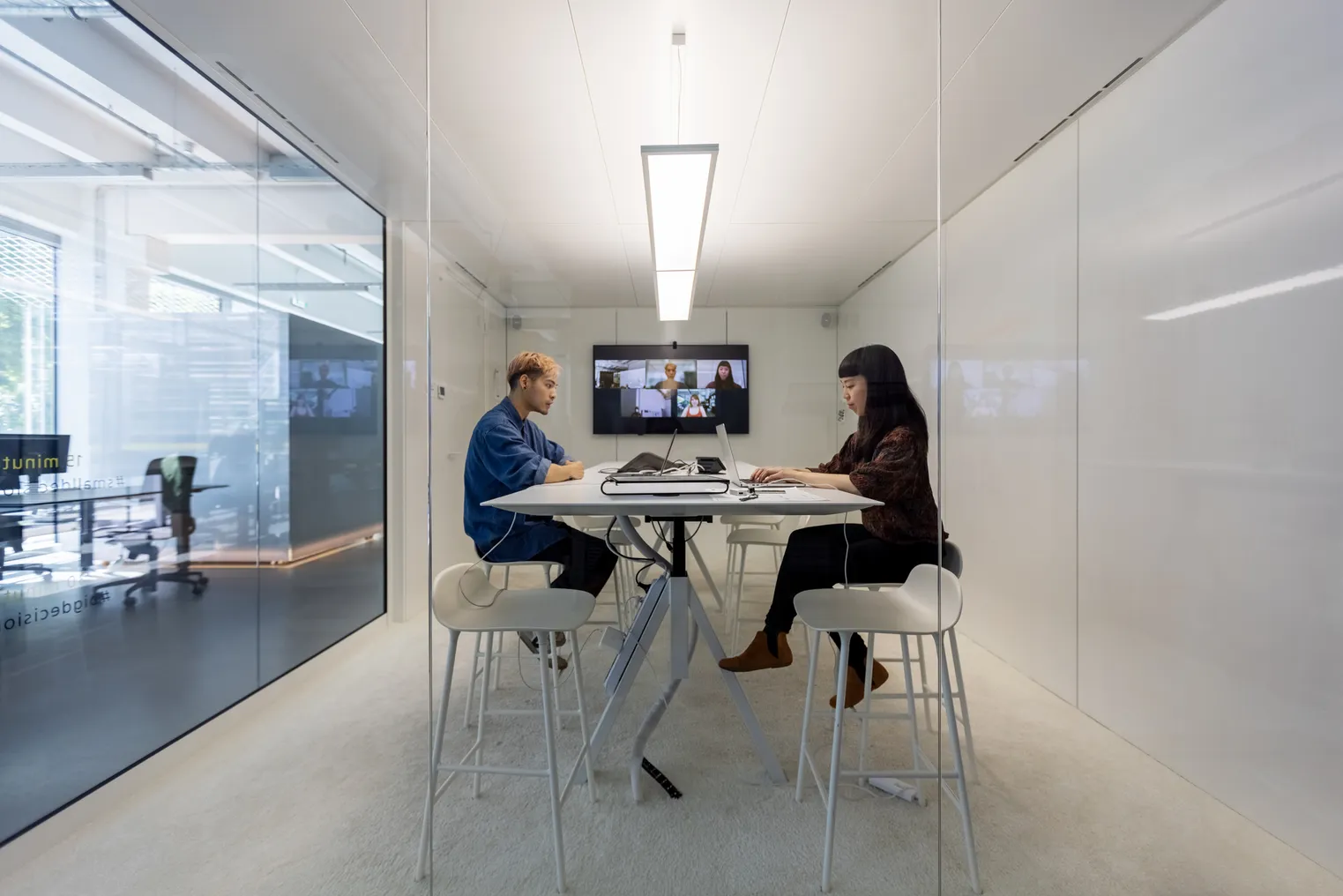 Two businesspeople sitting inside a small cubicle and working on their laptops. Man and woman working in hybrid office cubicle.