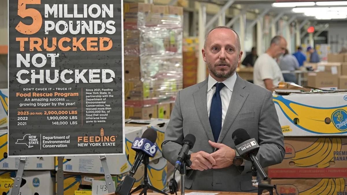 A man stands in a food recovery facility next to a sign that sayd "5 million pounds trucked not chucked"