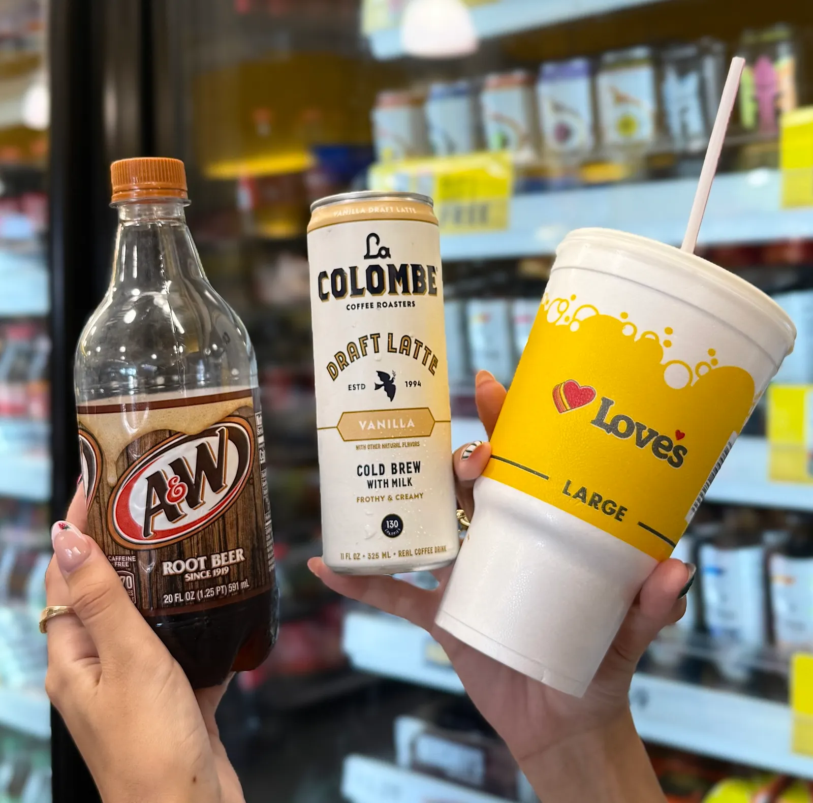 A photo of a person's hands holding a bottle of A&W eoor beer, a can of La Colombe coffee and a large Love's cup.