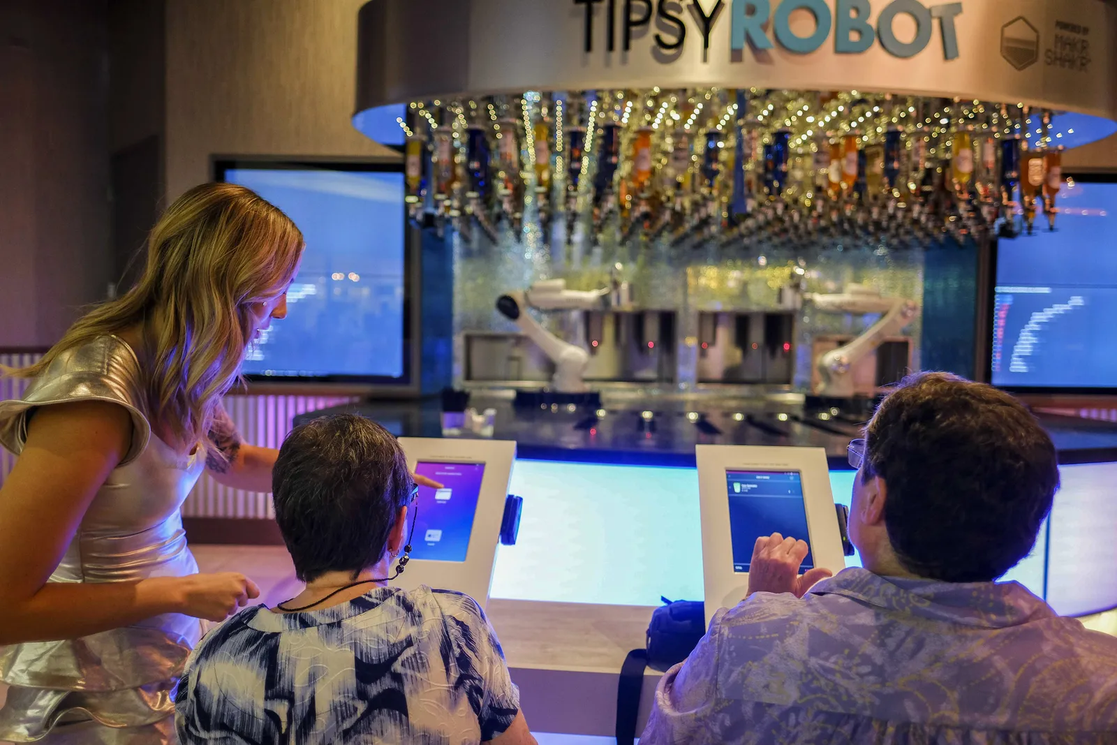 People use touch screens to order as robotic arms in the background appear to make drinks.