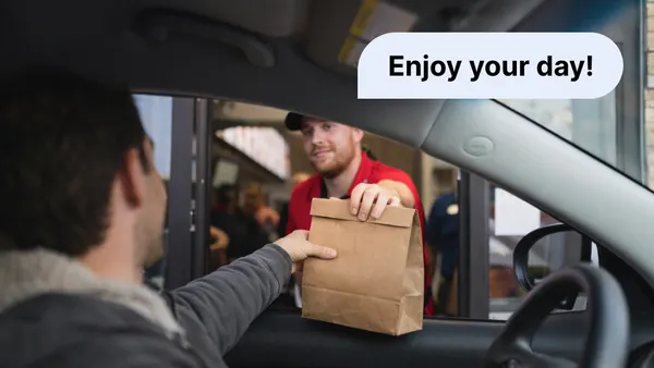 A photograph of a fast food employee handing a paper bag to a person in a car.