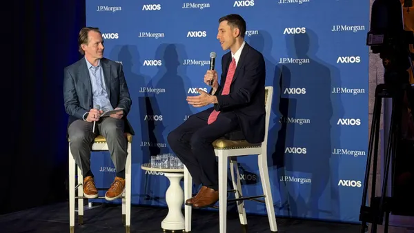 Two people sitting on stools on a stage converse.