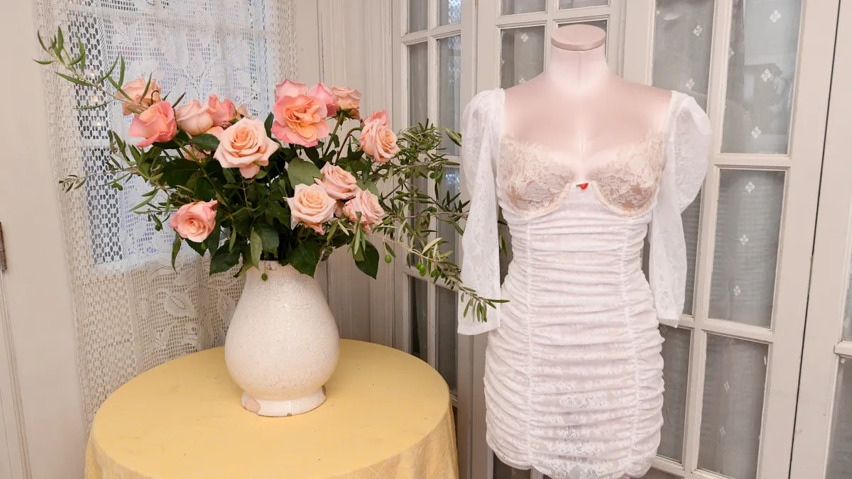 A piece of lingerie is displayed on a mannequin next to a bouquet of flowers.