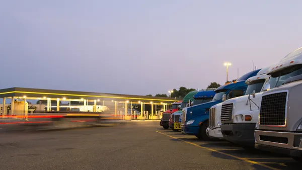 Trucks of various models and colors at a truck stop with a lit gas station.