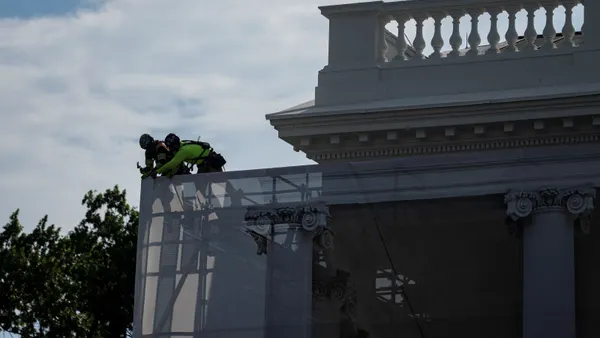 Two construction workers put tarp over scaffolding.