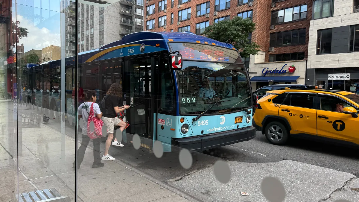 People board a bus at a with a yellow taxi driving by.