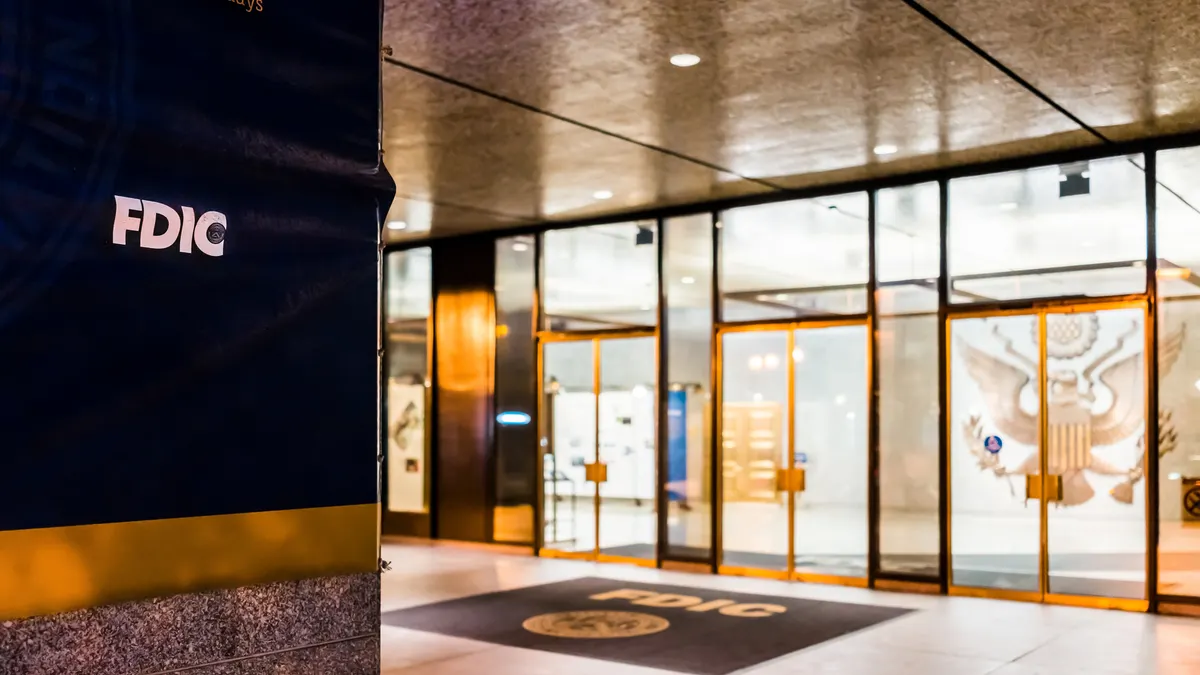 A sign shows the FDIC acronym in the foreground on the left, and glass doors and an FDIC rug in the background to the right.
